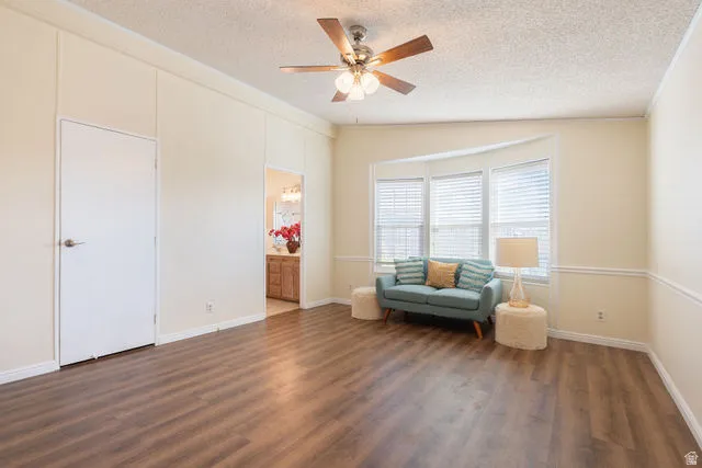 Wood-finish flooring, ceiling fan, bay windows with blinds, chair rail molding, and an attached bathroom with a wood-finish vanity