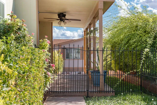 Covered patio with a ceiling fan, supported by wood posts, and secured with a black metal fence