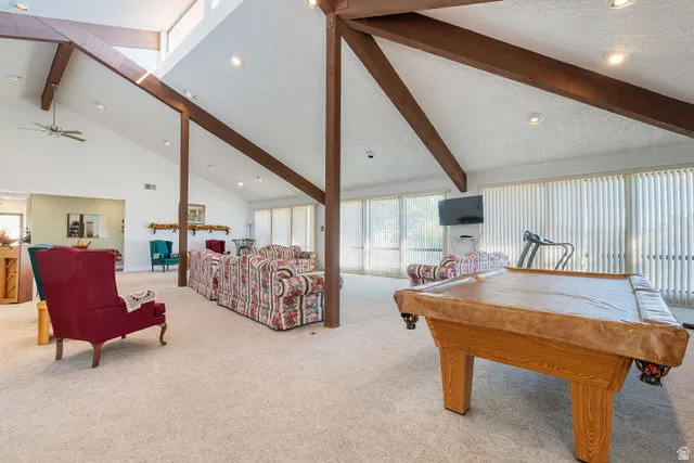 Vaulted ceilings with exposed wood beams, expansive window walls with vertical blinds, recessed lighting, and a ceiling fan