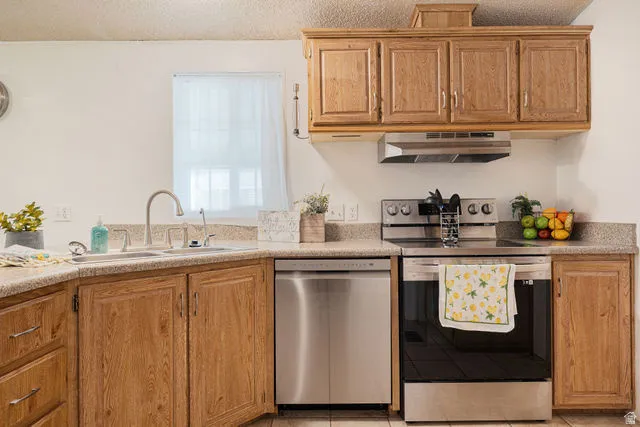Kitchen featuring wood-finish cabinetry, stainless steel appliances, a double basin sink with a gooseneck faucet, and light-toned countertops