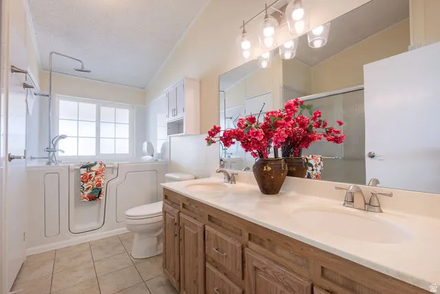 Bathroom featuring a double vanity with wood-finish cabinetry, a large integrated mirror, a walk-in tub with an overhead shower, and tile flooring