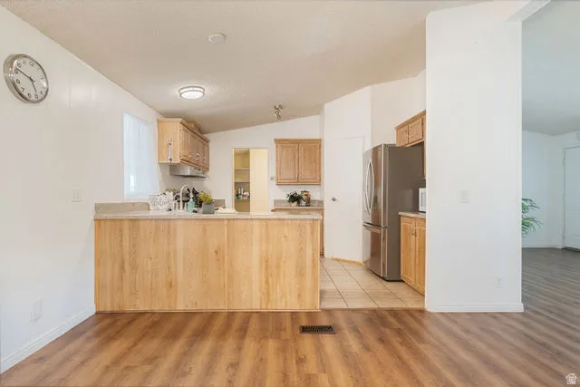 Wood-finish flooring throughout, light wood cabinetry, and a kitchen island with a stone-finish countertop
