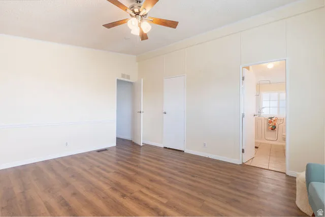 Spacious interior with wood-finish flooring, a ceiling fan with integrated lighting, and multiple doorways