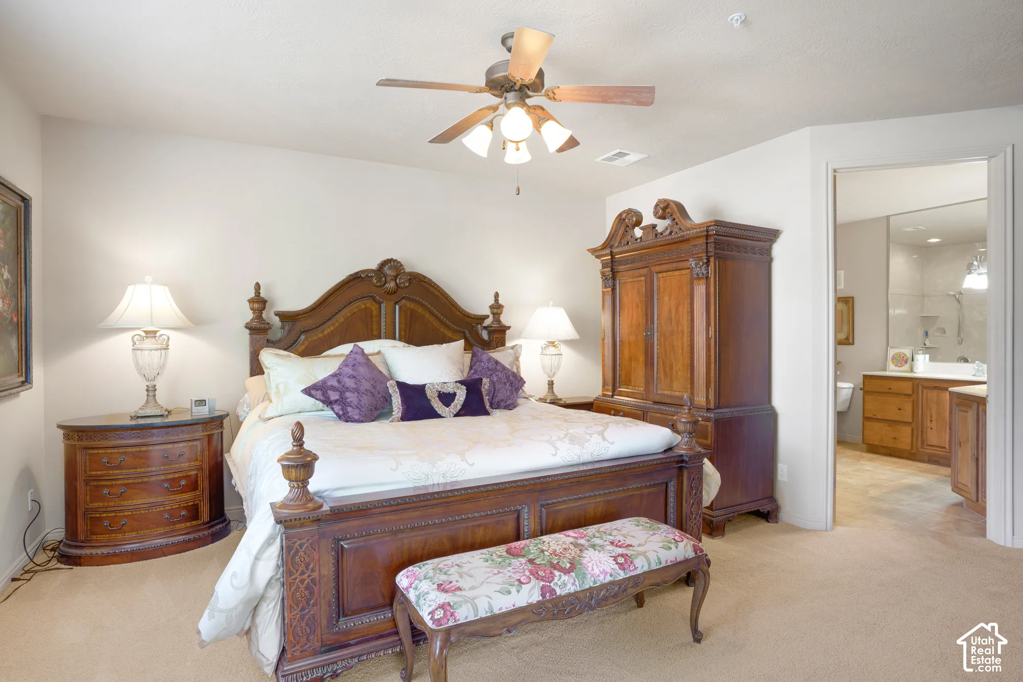 Carpeted flooring, ceiling fan with integrated lighting, and an open doorway leading to a bathroom with a dual vanity