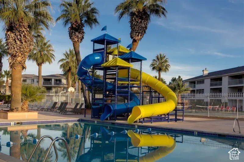 Pool area featuring a multi-level water slide structure, multiple palm trees, and a perimeter fence