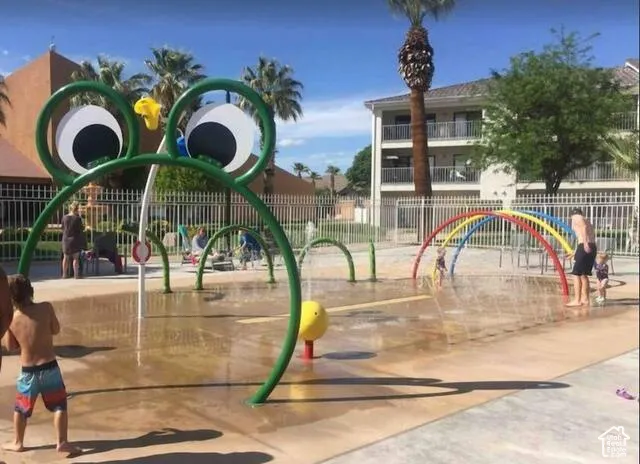 Splash pad with multiple water features, including a frog-themed sprayer and rainbow arches, on a concrete surface