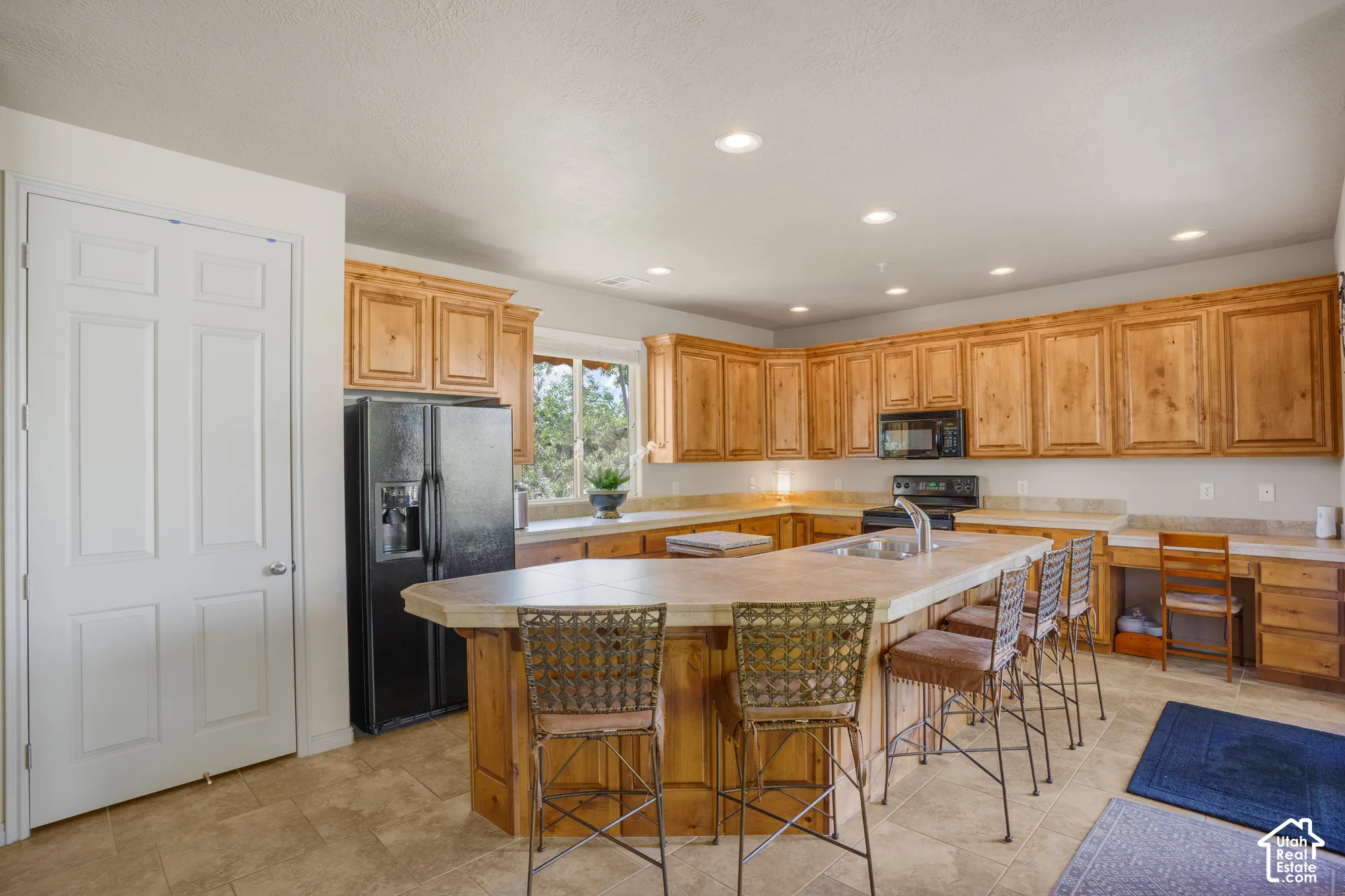 Kitchen featuring wood cabinetry, recessed lighting, a built-in desk area, a large island with seating, and tile flooring