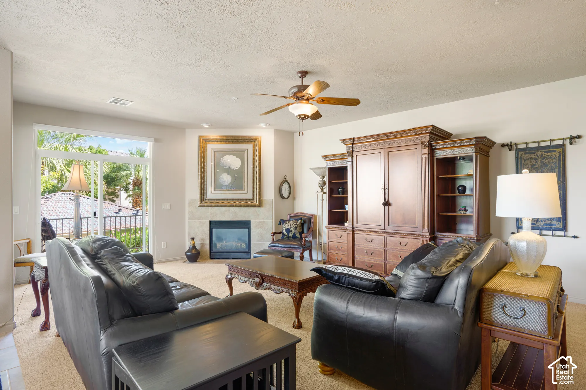 Living area with a corner fireplace featuring a tile surround and mantel, a ceiling fan, and sliding glass doors leading to an outdoor space