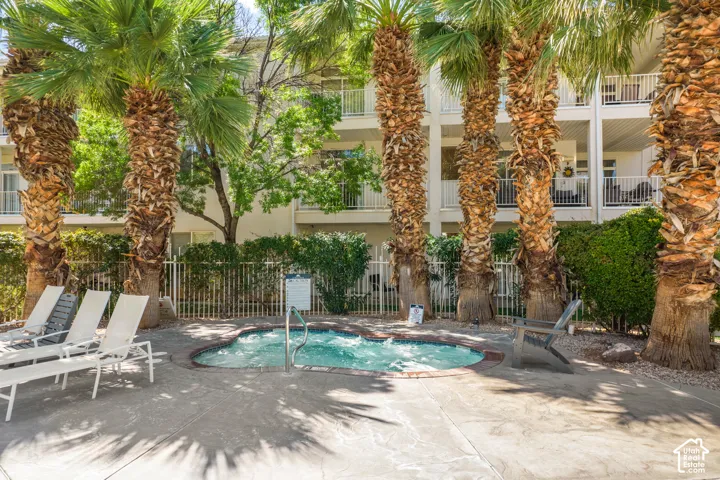 Outdoor hot tub with perimeter hardscaping, surrounded by lush palm trees, and privacy fencing