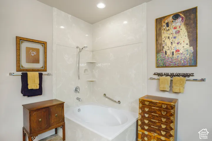 Built-in corner tub with a shower fixture, integrated shelving, and a grab bar