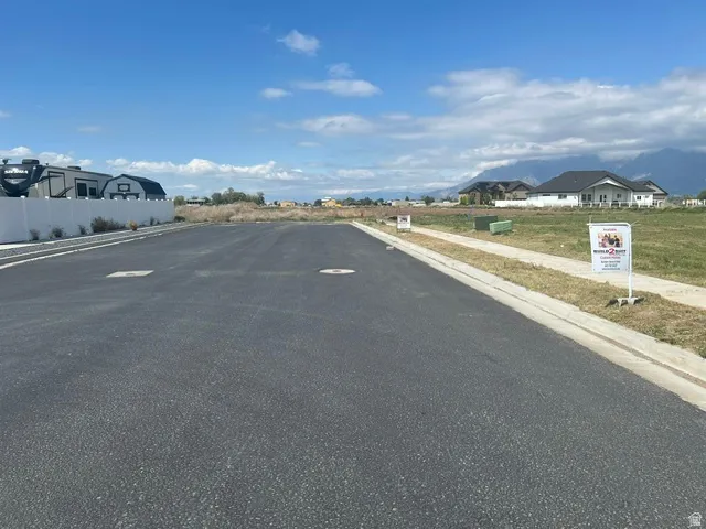 Paved road with integrated utility access points, concrete curb and sidewalk, and a white privacy fence