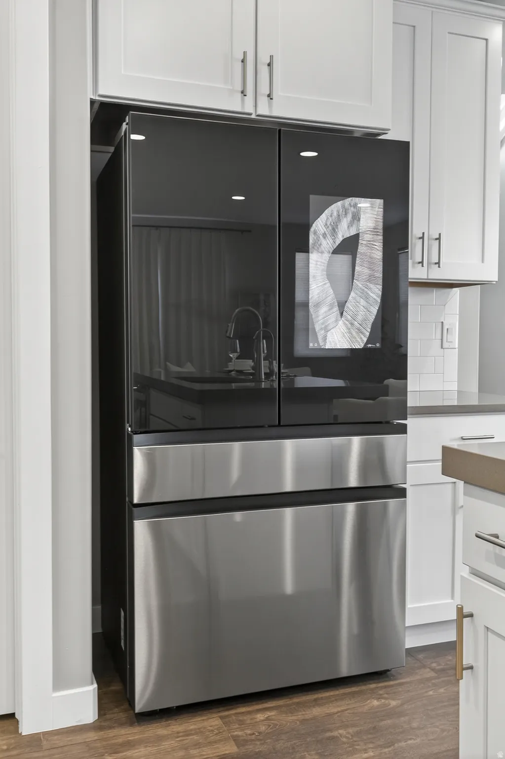 Integrated refrigerator with black glass and stainless steel finishes, white shaker cabinetry, wood-finish flooring, and white subway tile backsplash
