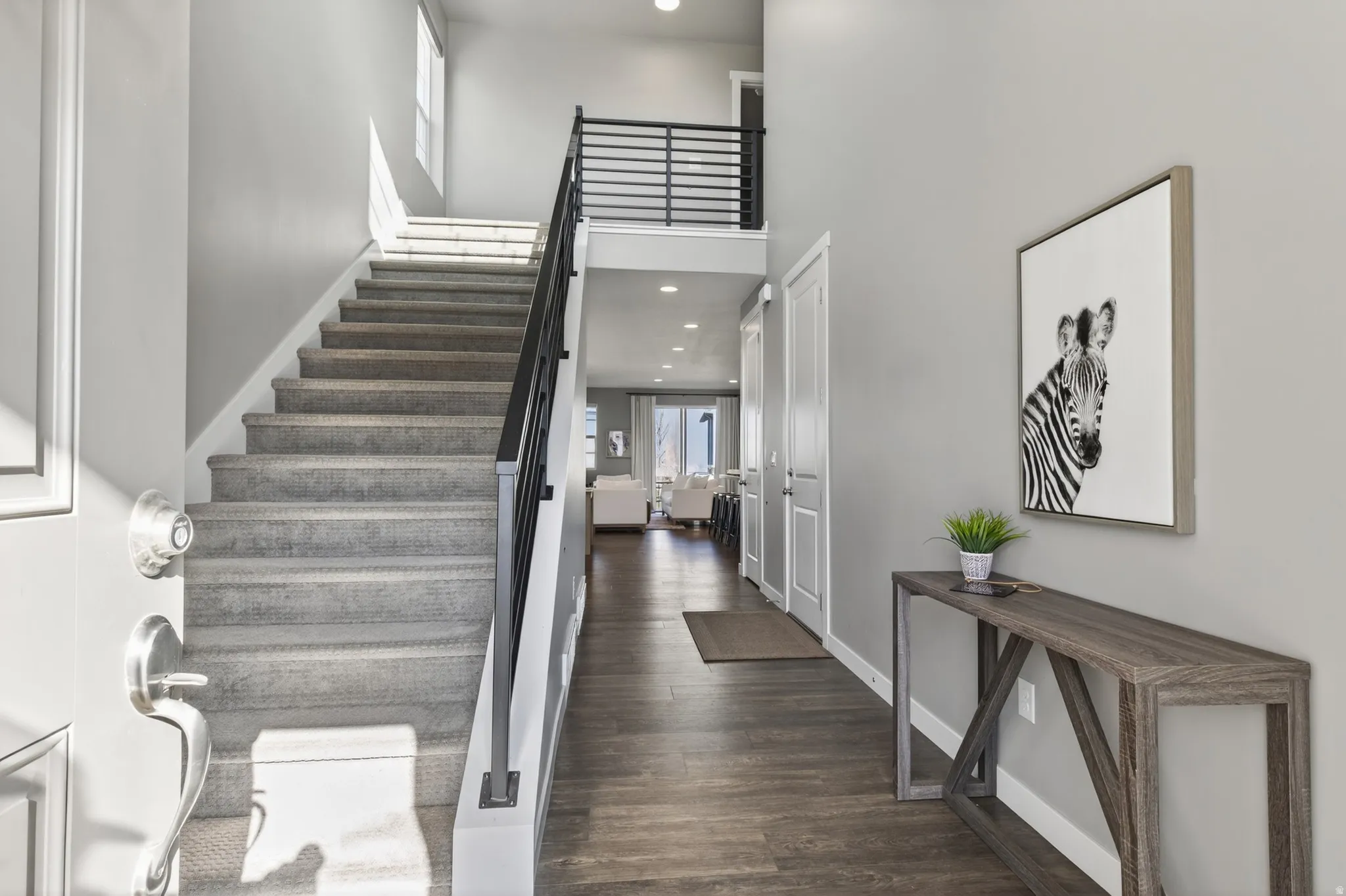 Two-story foyer with wood-finish flooring, carpeted staircase, and an open upper-level hallway with a black metal railing