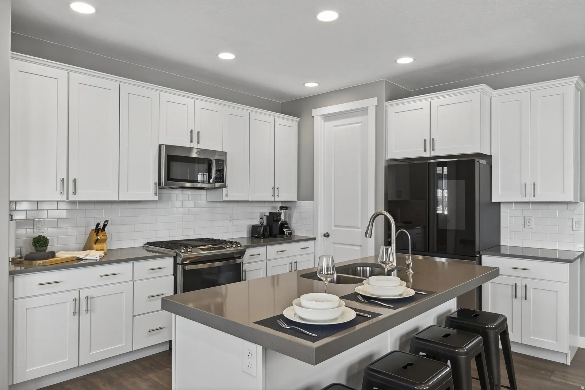 Kitchen with white shaker cabinetry, stainless steel appliances, a subway tile backsplash, and a large center island with a double basin sink
