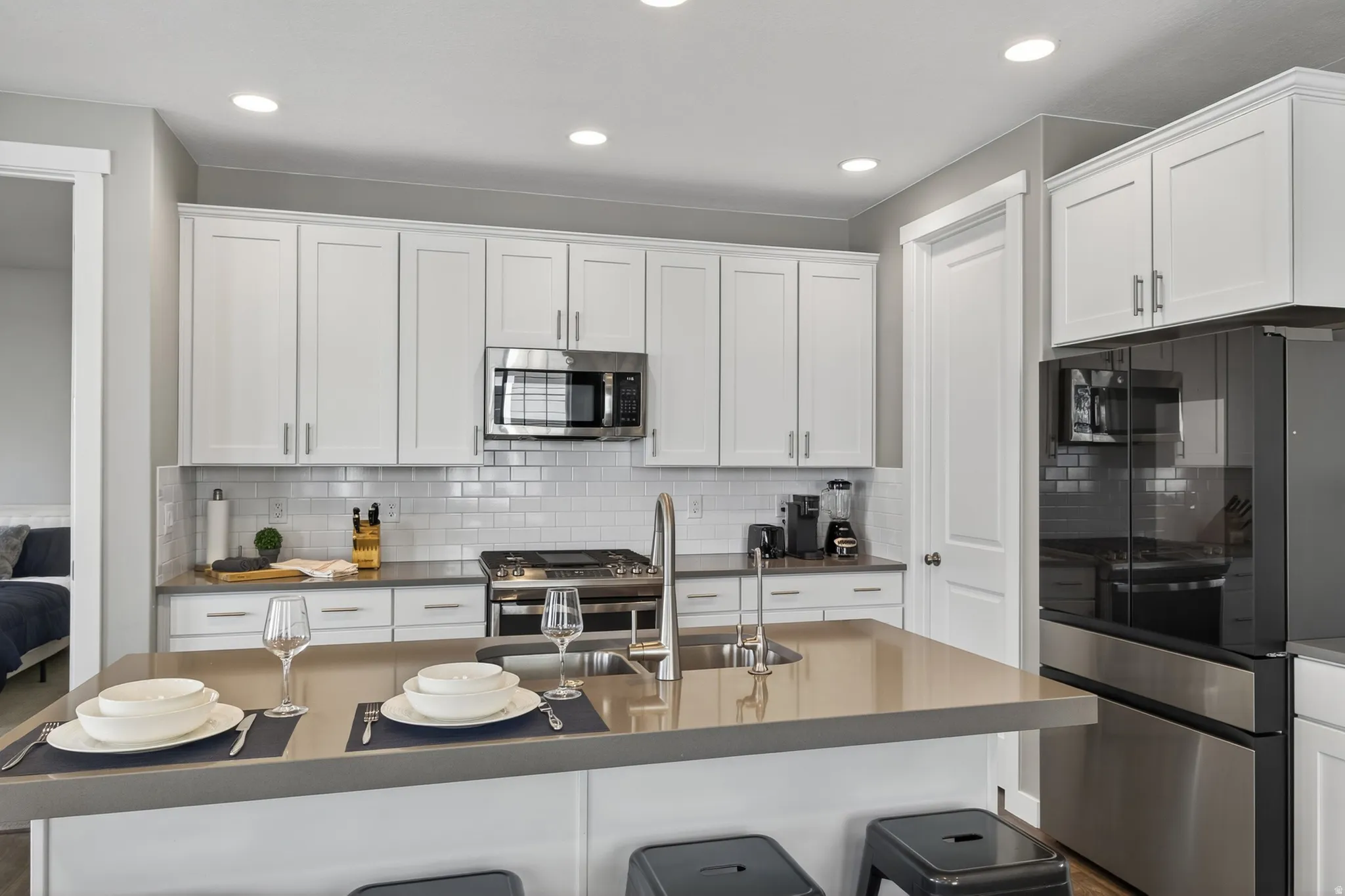 Modern kitchen featuring white shaker-style cabinetry, a subway tile backsplash, stainless steel appliances, recessed lighting, and a kitchen island with an undermount sink