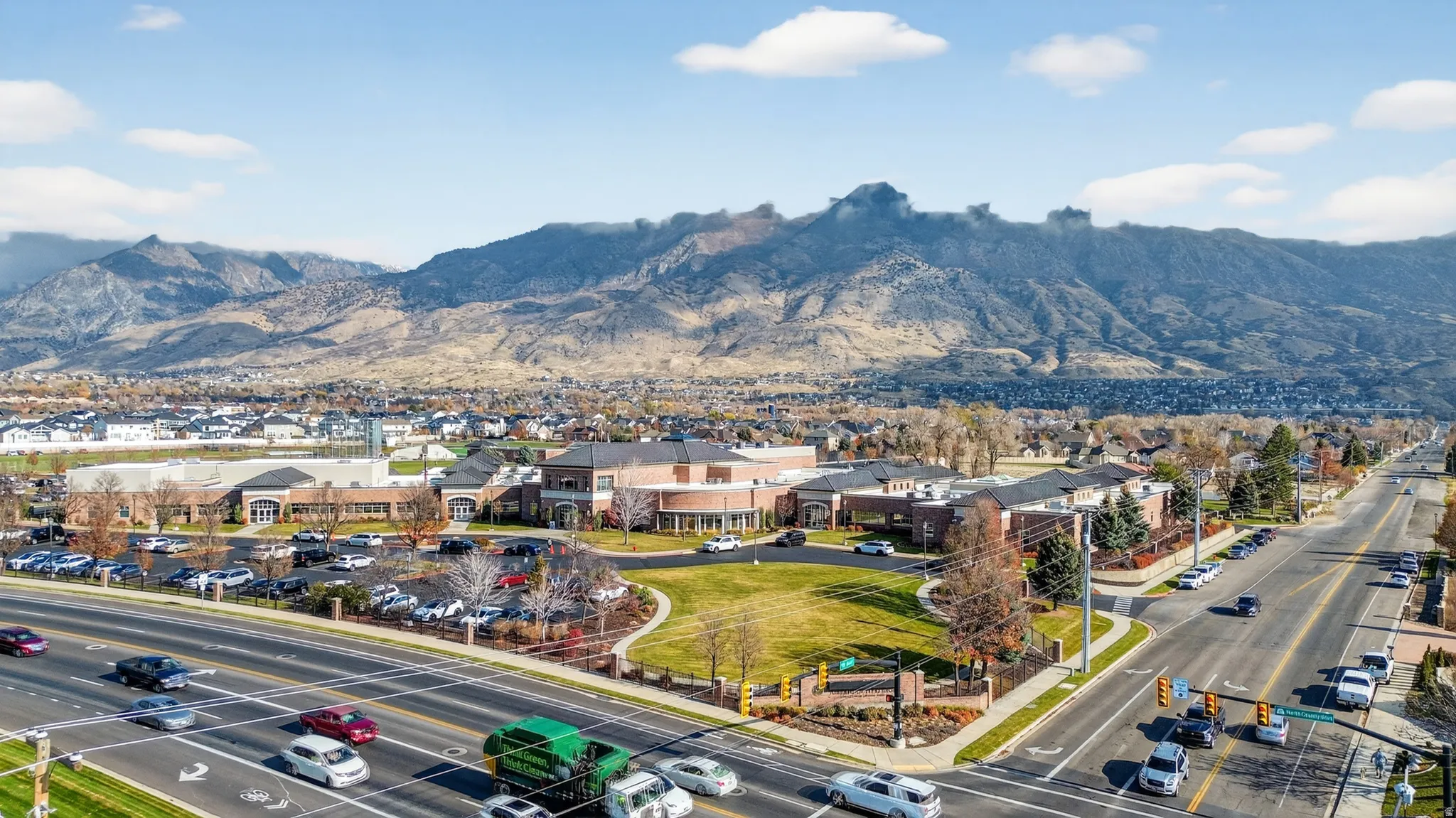Expansive mountain backdrop with a substantial commercial building, extensive paved parking areas, and mature landscaping