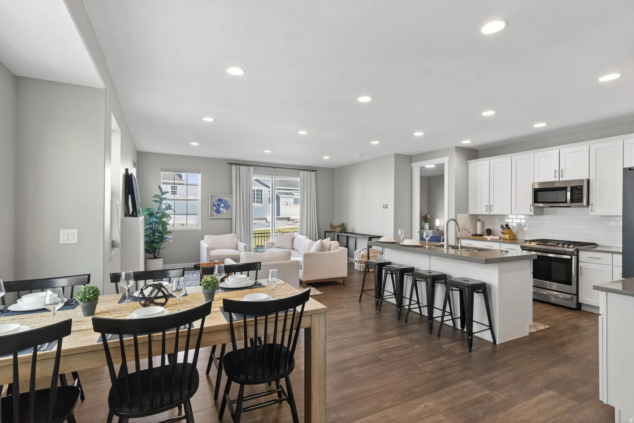 Wood-finish flooring throughout, white cabinetry, stainless steel appliances, recessed lighting, and a kitchen island with a sink