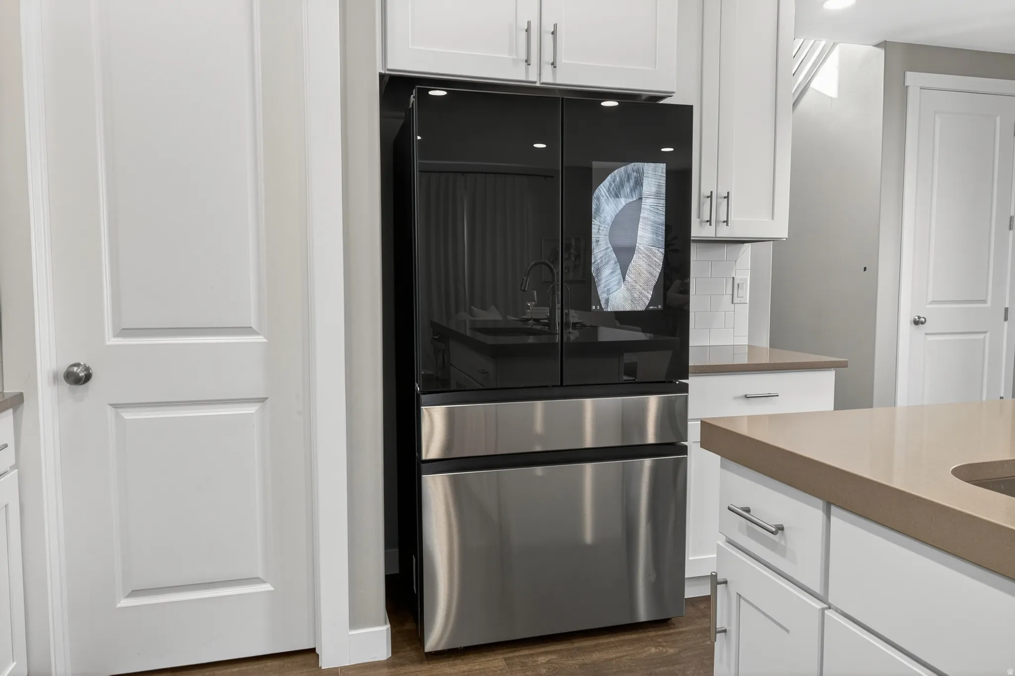 Built-in stainless steel and black glass refrigerator, white shaker-style cabinetry, light subway tile backsplash, and light-toned countertops