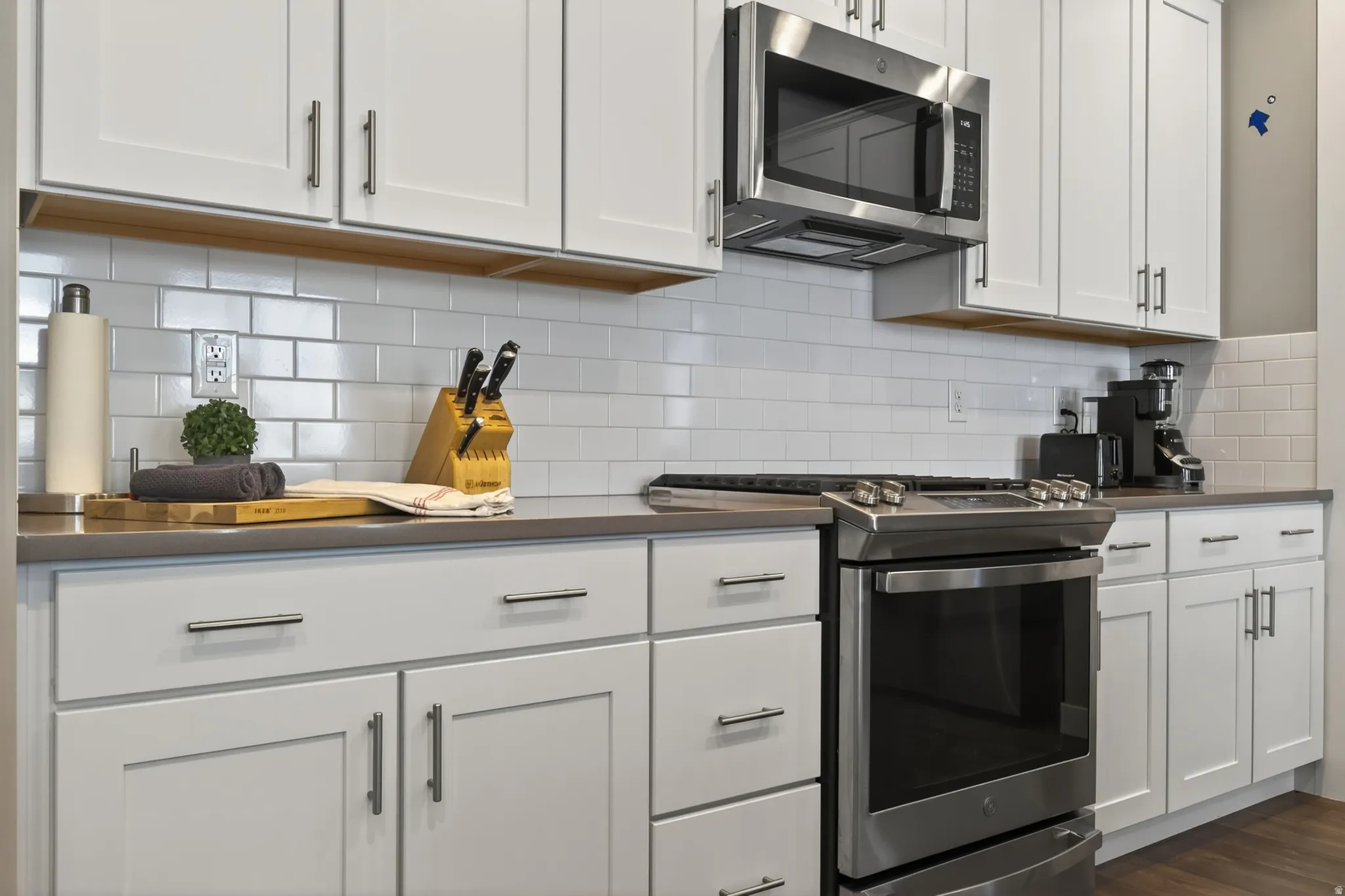 White shaker-style cabinetry, subway tile backsplash, stainless steel appliances, and dark countertops