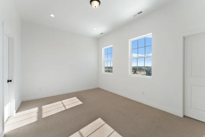 Two windows with grid patterns, recessed ceiling lights, a ceiling-mounted fixture, and light-colored carpeting