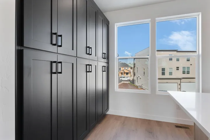 Full-height cabinetry with matte black hardware, dual windows, light-toned wood-finish flooring, and a white countertop