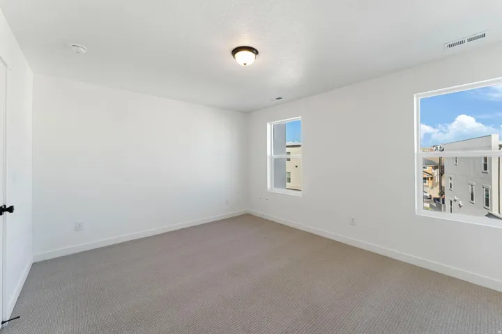 Wall-to-wall carpeting with white baseboards, two windows with white trim, a flush-mount ceiling light fixture, and a white interior door with black hardware