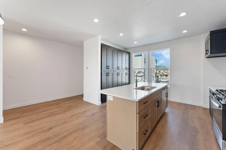 Kitchen featuring an island with a built-in sink, stainless steel appliances, dark cabinetry, and wood-finish flooring