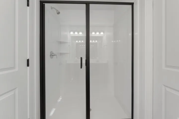 Shower enclosure with clear glass paneling and a black frame, featuring a built-in shower head and control handle
