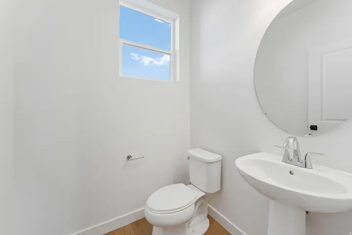 Pedestal sink with chrome faucet, circular wall-mounted mirror, and wood-finish flooring
