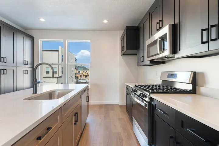 Kitchen featuring a gas range, stainless steel microwave, black cabinetry, wood-finish flooring, and a white countertop with an undermount sink