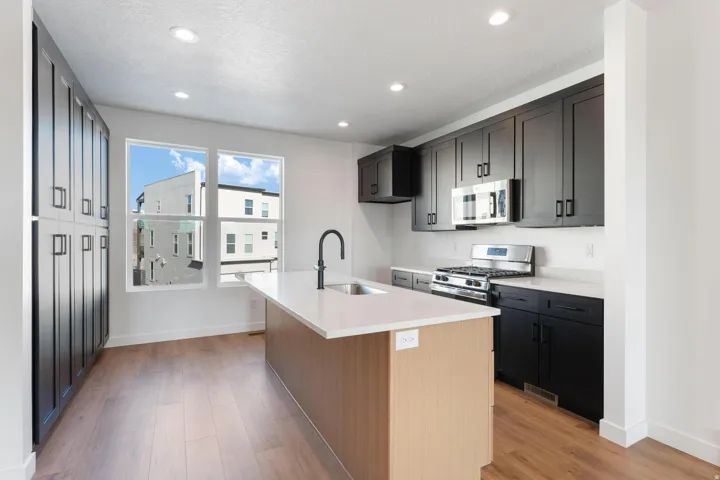 Kitchen featuring wood-finish flooring, dark cabinetry, light-toned countertops, a central island with an integrated sink, and stainless steel appliances