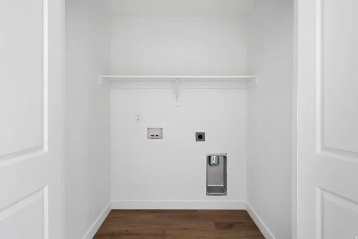 Dedicated laundry area featuring a white storage shelf, white walls, and wood-finish flooring