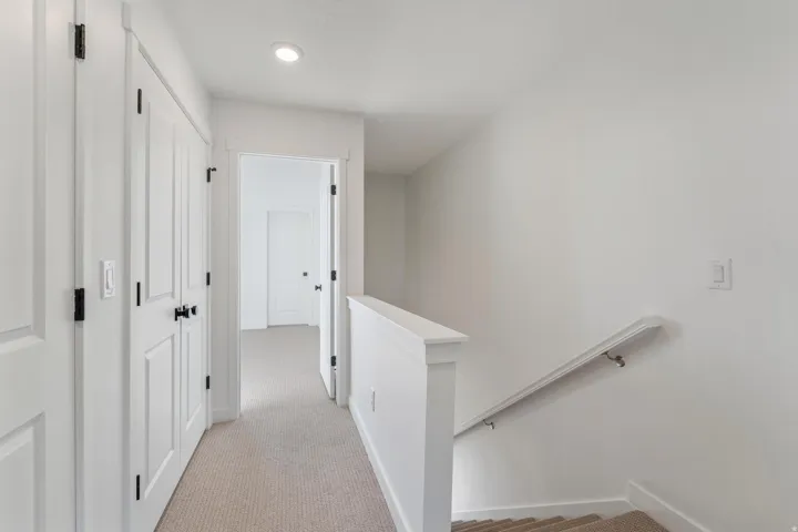 Neutral paint palette, recessed ceiling lighting, carpeted hallway, contrasting dark hardware, and a white stair railing