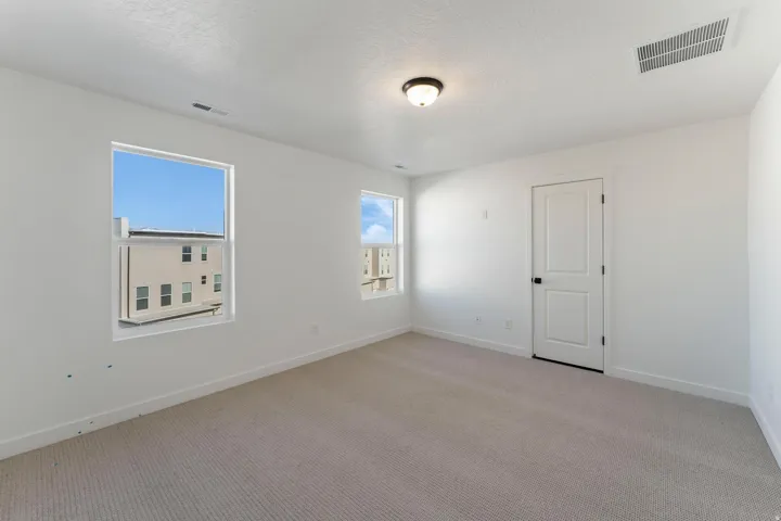 Neutral-toned carpeting with white walls, two windows, a white door, and a flush mount light fixture