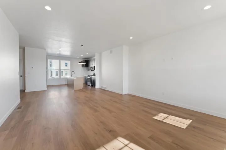 Open-concept living area with wood-finish flooring, recessed lighting, and a kitchen island featuring a black gooseneck faucet