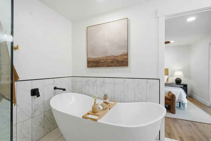 Freestanding soaking tub with matte black fixtures, white tile surround, and an open doorway