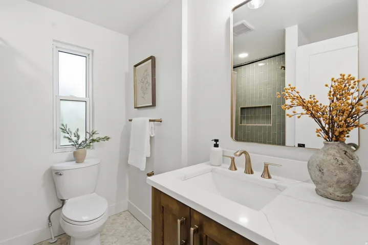 White rectangular undermount sink with a brass-finish widespread faucet, set in a light-toned countertop