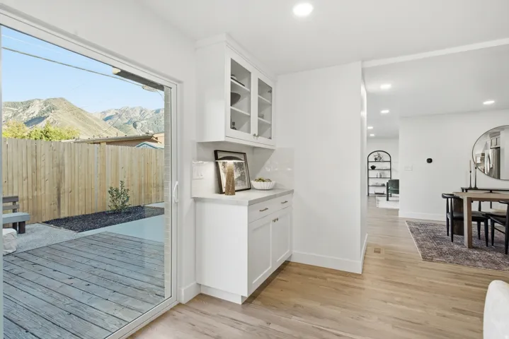 Sliding glass door leading to a wood-finish deck, custom built-in cabinetry with glass-front uppers, light wood-finish flooring, and recessed lighting