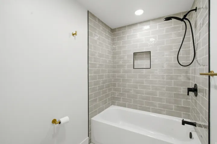 Bathtub with subway tile surround, recessed shower niche, and matte black fixtures
