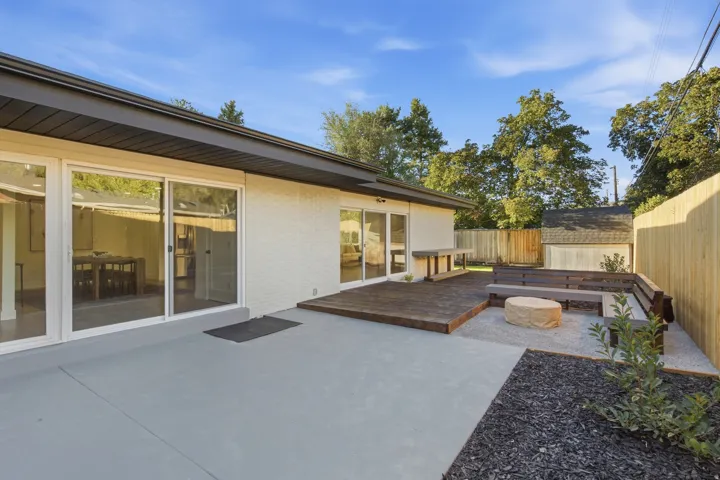 Expansive outdoor living area featuring a wood deck, concrete patio, gravel fire pit area, and a wood privacy fence