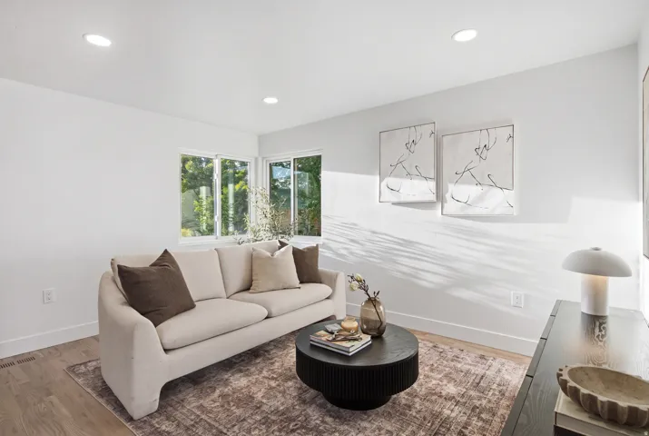 Recessed ceiling lighting illuminates a room with light wood-finish flooring and multiple windows