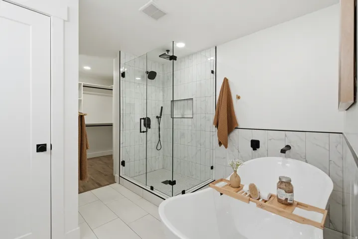 Walk-in shower with clear glass enclosure and black hardware, featuring a recessed niche and vertical tile