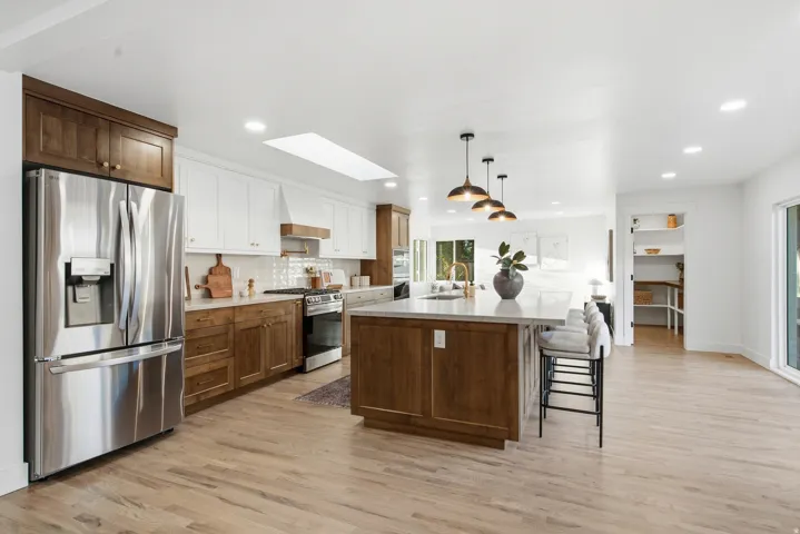 Spacious kitchen featuring wood-finish flooring, a kitchen island with seating, a skylight, a built-in pantry, and stainless steel appliances