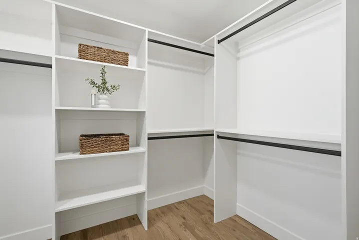 Built-in closet system featuring white shelving, black hanging rods, and wood-finish flooring