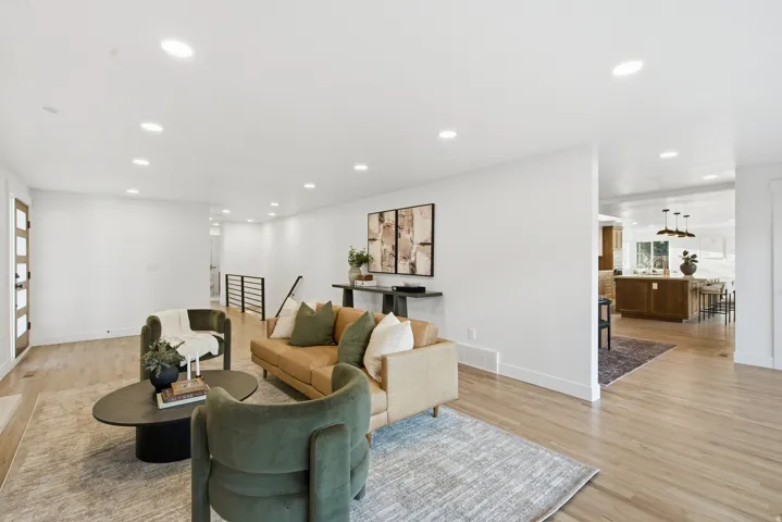 Recessed lighting, wood-finish flooring, white walls, black metal railing, and a modern wood-panel door