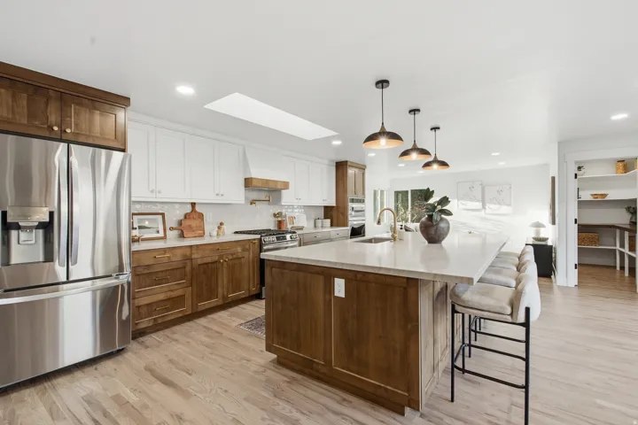 Spacious kitchen with a large central island, light wood-finish flooring, white upper cabinetry, and contrasting natural wood lower cabinetry