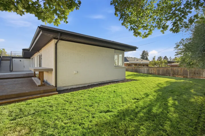 Expansive green lawn, wood-finish deck, exterior featuring stucco siding, multiple windows, and a black flat roof