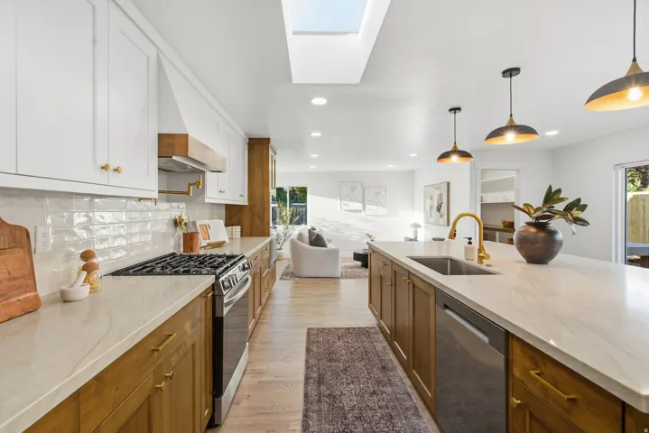 Kitchen featuring a skylight, white upper cabinetry, wood-finish lower cabinetry, a gas range, and a large island with an undermount sink