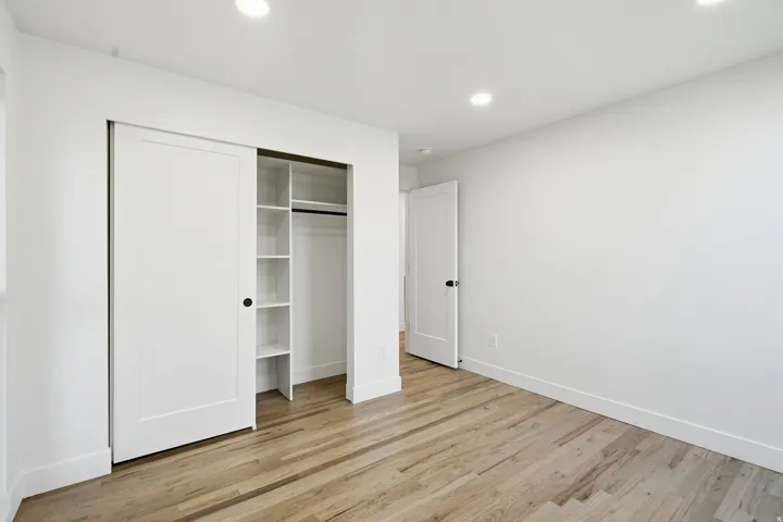 Light wood-finish flooring, recessed lighting, white walls, and a closet with built-in shelving