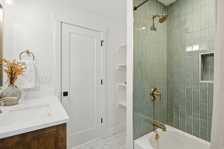 White vanity with integrated sink and countertop, white paneled door, and a tiled shower with a built-in niche and gold-toned fixtures